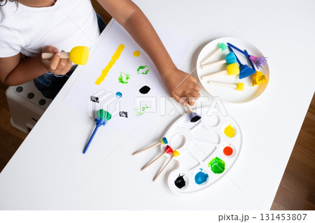Child engaging in creative painting with colorful art supplies on white table Child engaging in creative painting with colorful art supplies on white table 131453807
