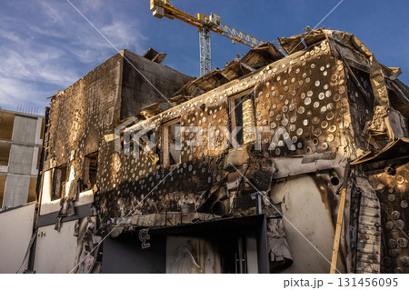 War. The aftermath of Russian airstrikes on a peaceful Ukrainian city. A hospital and a recreation center were destroyed. Severely burned building with warped facade and crane in daylight scene. War. The aftermath of Russian airstrikes on a peaceful Ukrainian city. A hospital and a recreation center were destroyed. Severely burned building with warped facade and crane in daylight scene. 131456095