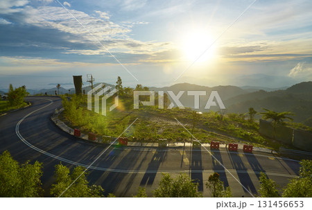 Winding mountain road at sunrise illuminating lush green valley Winding mountain road at sunrise illuminating lush green valley 131456653
