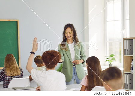 Schoolboy sitting at the desk raising hand up ready to answer in the classroom. 131456844