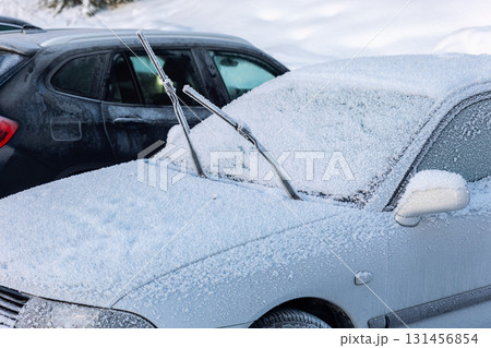 Car covered with snow and ice stands parked outdoors in cold winter weather. Windshield wipers are raised to prevent freezing, showing typical seasonal preparation 131456854
