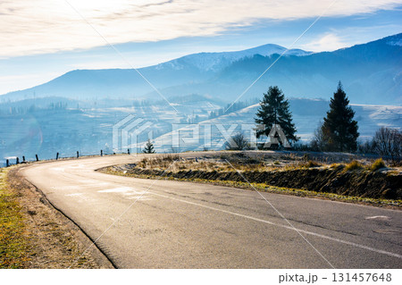 country road in carpathian mountains. beautiful landscape of ukraine in late autumn. fir trees on the roadside in morning light. scenic view of blue sky with clouds above the distant ridge in snow 131457648