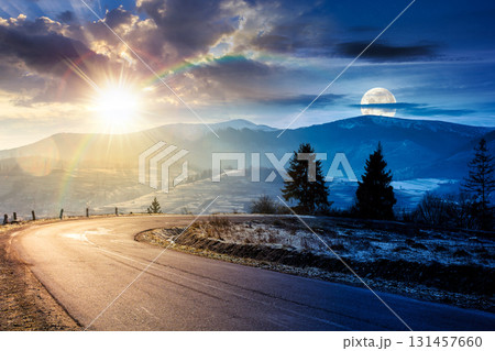 country road in mountains. day and night time change concept. beautiful countryside landscape in late autumn. fir trees on the roadside with sun and moon. scenic view of distant ridge in snow 131457660