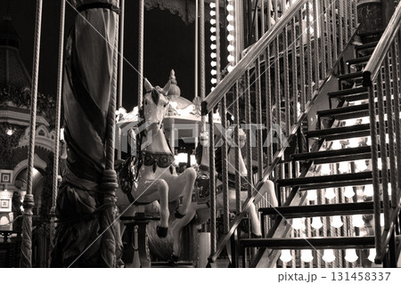 Black and white image of vintage carousel with illuminated lights and white horses. Photo captures nostalgic charm of old fashioned fair ride, evoking feelings of childhood memories and joy 131458337