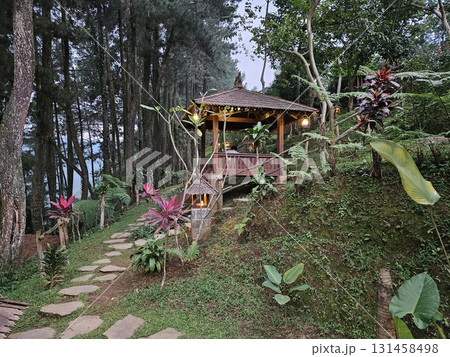 A close-up shot captures a single lit candle sitting on a wooden table next to a clear glass of water, casting a warm, intimate glow that creates a peaceful, softly lit atmosphere in the darkness. 131458498