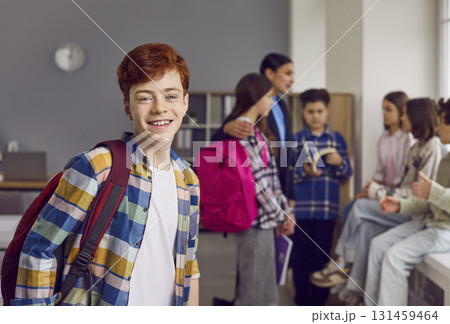 Portrait of smiling redhead boy standing with backpack in classroom Portrait of smiling redhead boy standing with backpack in classroom 131459464