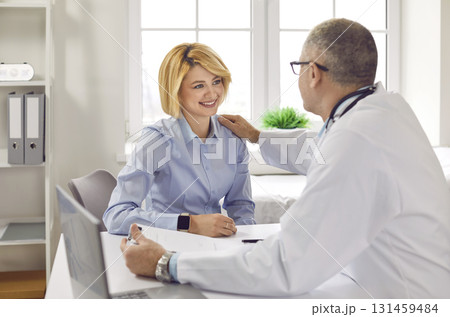 Senior male doctor talking about treatment and supporting his young woman patient Senior male doctor talking about treatment and supporting his young woman patient 131459484