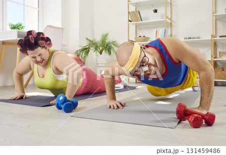 Funny couple pushing up lying on the floor on yoga mat in sportswear at home. 131459486