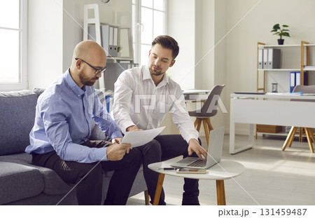 Two young business men sitting on sofa work in office talking and having discussion. Two young business men sitting on sofa work in office talking and having discussion. 131459487