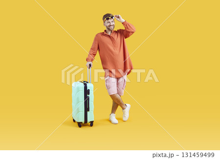 Happy male tourist in summer clothes standing with his suitcase on yellow background 131459499