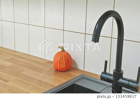 Minimalist kitchen with black faucet and small pumpkin on wooden counter against white tiles Minimalist kitchen with black faucet and small pumpkin on wooden counter against white tiles 131459617