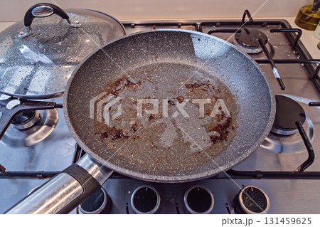 Greasy non stick pan on gas stove after cooking, brown residue in center, cleanup pending 131459625