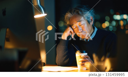 男性が夜のオフィスで疲れてコーヒーを手に休む 131459995