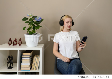Woman using smartphone with headphones in a cozy home setting 131460034