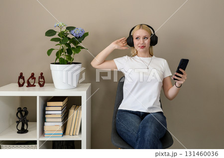 Woman listening to music on headphones while holding smartphone Woman listening to music on headphones while holding smartphone 131460036