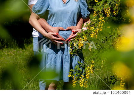 Pregnant couple forming heart shape on belly in blooming garden 131460094