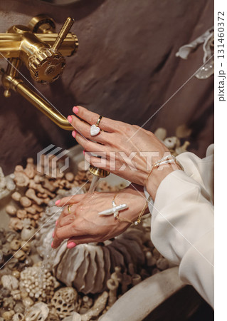 Young woman washing hands at seashell-decorated washbasin with fashionable pearl beads Young woman washing hands at seashell-decorated washbasin with fashionable pearl beads 131460372