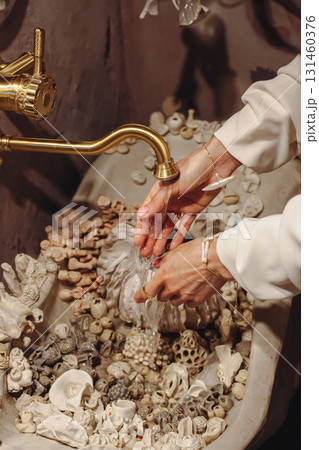 Young woman washes her hands in a seashell decorated washbasin with unique pearl beads Young woman washes her hands in a seashell decorated washbasin with unique pearl beads 131460376