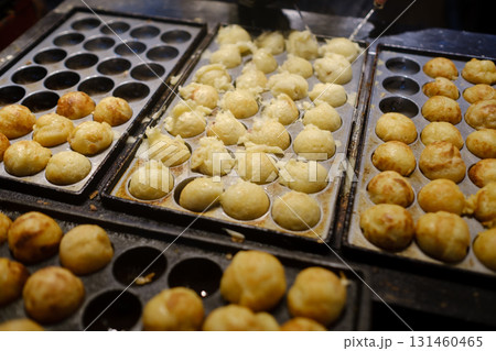 Takoyaki being cooked on a hot griddle at a street food stall during a bustling night market in Japan Takoyaki being cooked on a hot griddle at a street food stall during a bustling night market in Japan 131460465