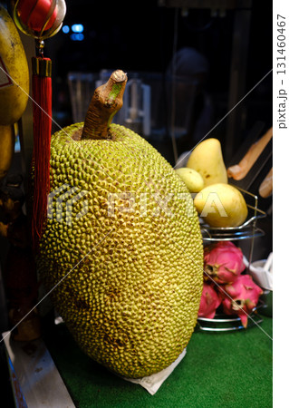 Large jackfruit displayed on a countertop at a market, showing its unique texture and vibrant color alongside other ripe fruits in an evening setting 131460467