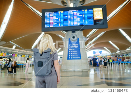 Traveler waits at airport terminal and looks at flight information board with a backpack during afternoon Traveler waits at airport terminal and looks at flight information board with a backpack during afternoon 131460478
