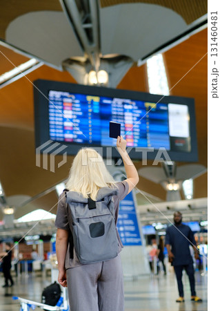 Passenger checks flight details at an airport terminal while holding a passport in the air and preparing for travel during a sunny day 131460481