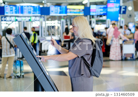 Woman interacts with self-service kiosk at busy airport terminal while checking in for her flight during the day 131460509