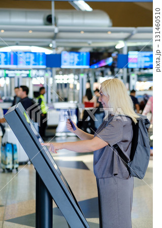 Traveler uses self-check-in kiosk at busy airport while preparing for upcoming flight to an international destination 131460510