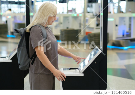 Woman using self-check-in kiosk at airport terminal while preparing for an upcoming flight in a busy travel environment Woman using self-check-in kiosk at airport terminal while preparing for an upcoming flight in a busy travel environment 131460516