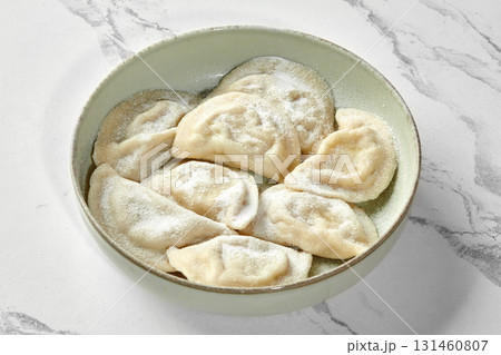 Vareniki or dumplings with potato sprinkled with flour in ceramic bowl on marble table background 131460807