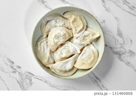 Delicious polish dumplings, pierogi, sprinkled with powdered sugar, resting in a bowl on marble surface 131460808