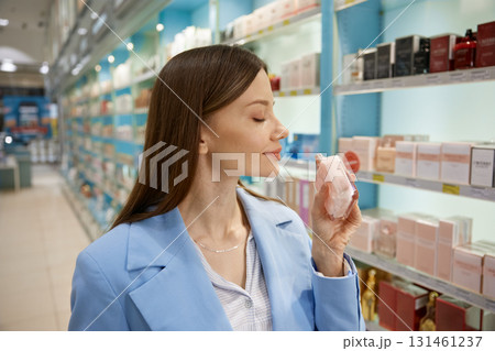 A woman is actively smelling a bottle of perfume that she found in a store A woman is actively smelling a bottle of perfume that she found in a store 131461237