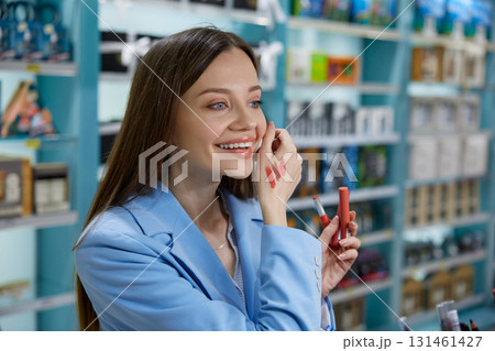 A woman is carefully applying lipstick to her lips while in a store nearby A woman is carefully applying lipstick to her lips while in a store nearby 131461427