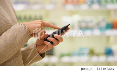 Close-up of female hands reading the label of a skincare product in a beauty store. Customer checking ingredients while choosing a moisturizer. Concept of conscious self-care and product selection. Close-up of female hands reading the label of a skincare product in a beauty store. Customer checking ingredients while choosing a moisturizer. Concept of conscious self-care and product selection. 131461883
