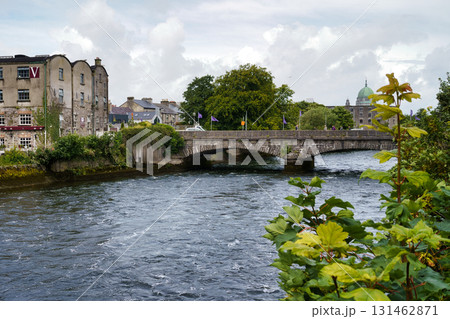 A scenic view of a bridge over a river in a town, featuring historic buildings and lush greenery under a cloudy sky in Ireland. A scenic view of a bridge over a river in a town, featuring historic buildings and lush greenery under a cloudy sky in Ireland. 131462871