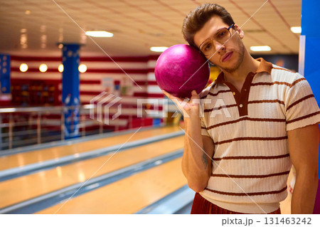 Man in striped shirt holding purple bowling ball beside face Man in striped shirt holding purple bowling ball beside face 131463242