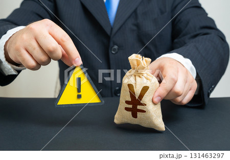 A man with a sign of attention and a yen or yuan money bag. Restrictions, monetary policy. Sanctions, budget deficit, emergency fund. Useful for finance, banking, trade, economy and risk management. 131463297