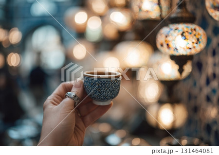 Hand holding small coffee cup with silver agate ring, hanging lanterns and mosaic tiles background 131464081