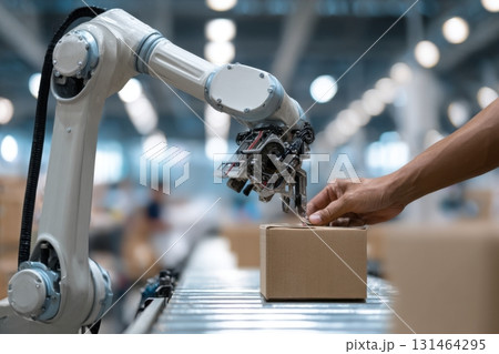 Human hand placing item into robotic gripper showing human-robot interaction in modern logistics 131464295