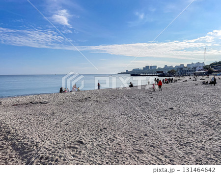 People enjoying a sunny day on a sandy beach with a calm sea and distant city skyline, perfect for leisure, family holidays, and seaside recreation 131464642