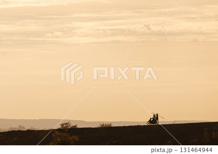 Silhouette of two men biker and a motorcycle on the road with sunset light background Silhouette of two men biker and a motorcycle on the road with sunset light background 131464944