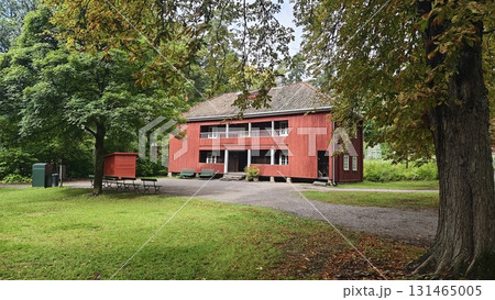 Traditional red wooden house surrounded by lush greenery and trees in a peaceful park setting. 131465005
