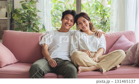 Positive happy young husband and wife relaxing on a cozy pastel-colored couch, surrounded by soft natural light, enjoying warm moments together 131465137