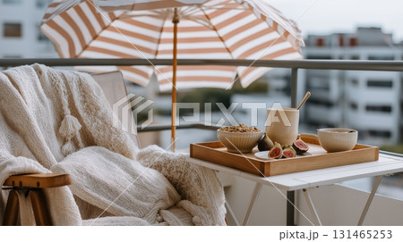 Cozy balcony breakfast setup with figs, granola and hot drink next to a knit blanket and umbrella 131465253