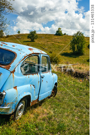 Side view of a blue damaged car abandoned on rolling grassy hills, surrounded by natural landscape, highlighting rustic rural scenery and dramatic automotive scene ideal for travel, lifestyle, and Side view of a blue damaged car abandoned on rolling grassy hills, surrounded by natural landscape, highlighting rustic rural scenery and dramatic automotive scene ideal for travel, lifestyle, and 131465338