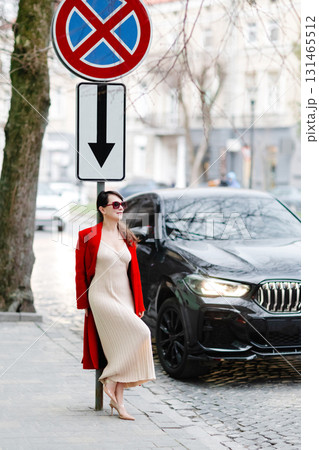 Stylish woman hailing a cab on a city street, wearing a red coat and sunglasses 131465512