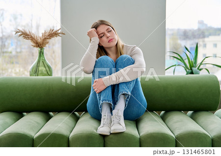 Unhappy upset young woman sitting on sofa at home, face close-up Unhappy upset young woman sitting on sofa at home, face close-up 131465801