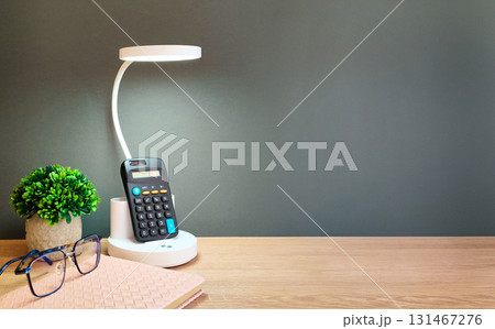 On the table there is a lamp, a calculator, a flower, a notebook and glasses On the table there is a lamp, a calculator, a flower, a notebook and glasses 131467276