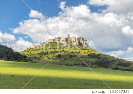 Spis Castle in Slovakia, Europe. Historic castle atop a verdant hill under a cloudy blue sky, evoking a sense of timelessness and fairytale charm. 131467323
