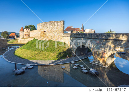 Bardejov town in North-Eastern Slovakia, Europe. Picturesque view of an old stone fortress with a bridge and waterway under a clear blue sky, showcasing historical architecture. Bardejov town in North-Eastern Slovakia, Europe. Picturesque view of an old stone fortress with a bridge and waterway under a clear blue sky, showcasing historical architecture. 131467347